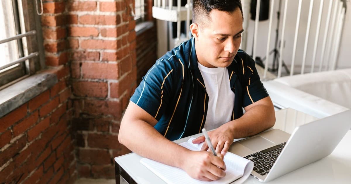 Student writing notes while attending an online BIM course on a laptop